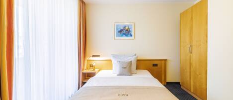 A hotel room with a bed, a nightstand, a lamp, a painting on the wall, and a wardrobe.