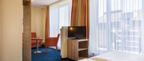 A hotel room with two beds, a desk with a TV, a small table, and a chair.