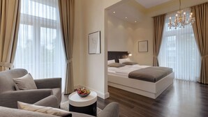 Una habitación de hotel moderna con una cama grande, una zona de estar con sofá y una mesita, y una araña.
