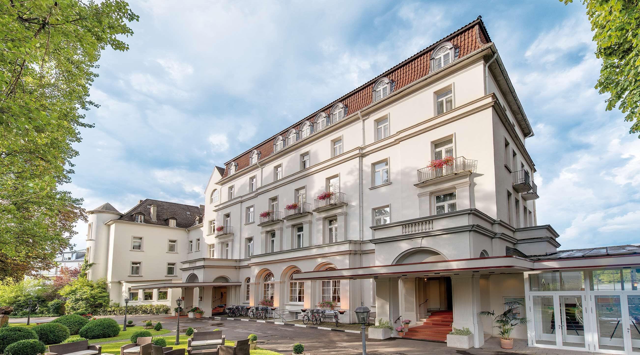 Un hotel de varios pisos con un patio central, que cuenta con una entrada cubierta, asientos al aire libre y un área de estacionamiento para bicicletas.