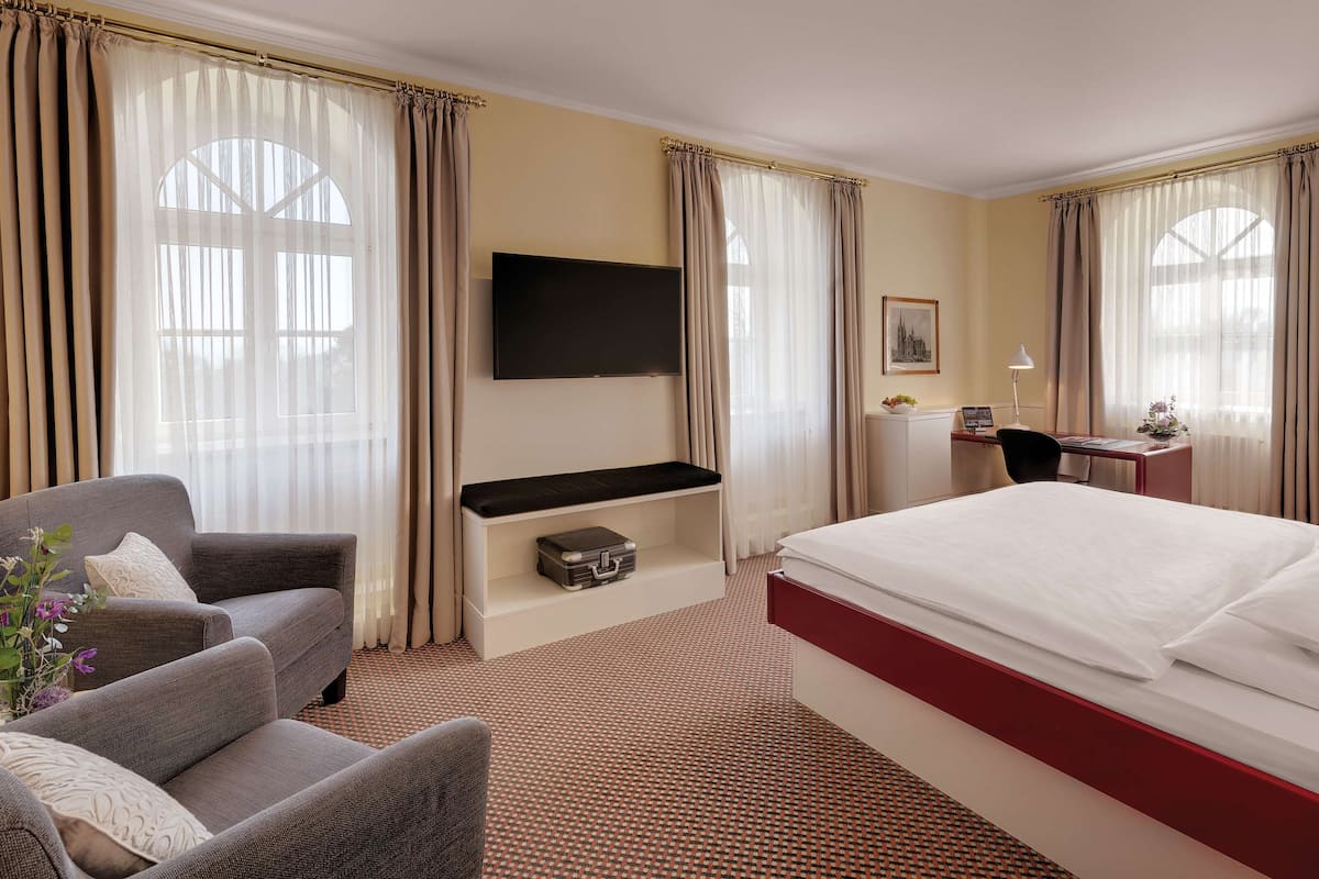 A hotel room with a bed, a desk, a chair, a TV, and curtains.