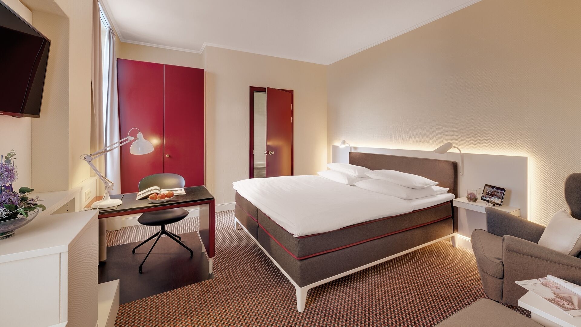 Una habitación de hotel con cama, escritorio, silla, lámpara y televisor.