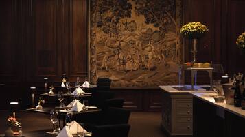A formal dining room with a large mural, wooden paneling, and a well-set dining table with chairs and a vase of flowers.