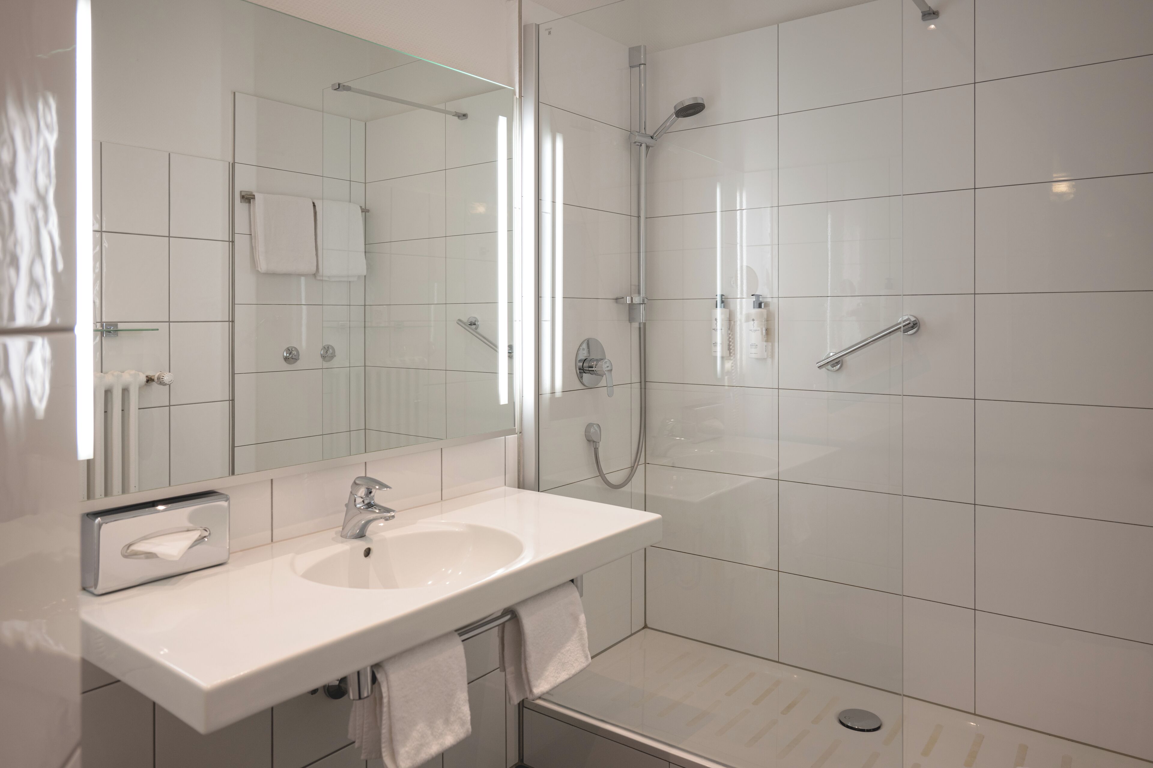 A modern bathroom with a white sink, mirror, and glass-enclosed shower.