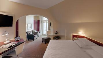 Hotelkamer met een bed, bureau, stoel, televisie en uitzicht door een boogvormige deuropening naar een balkon.