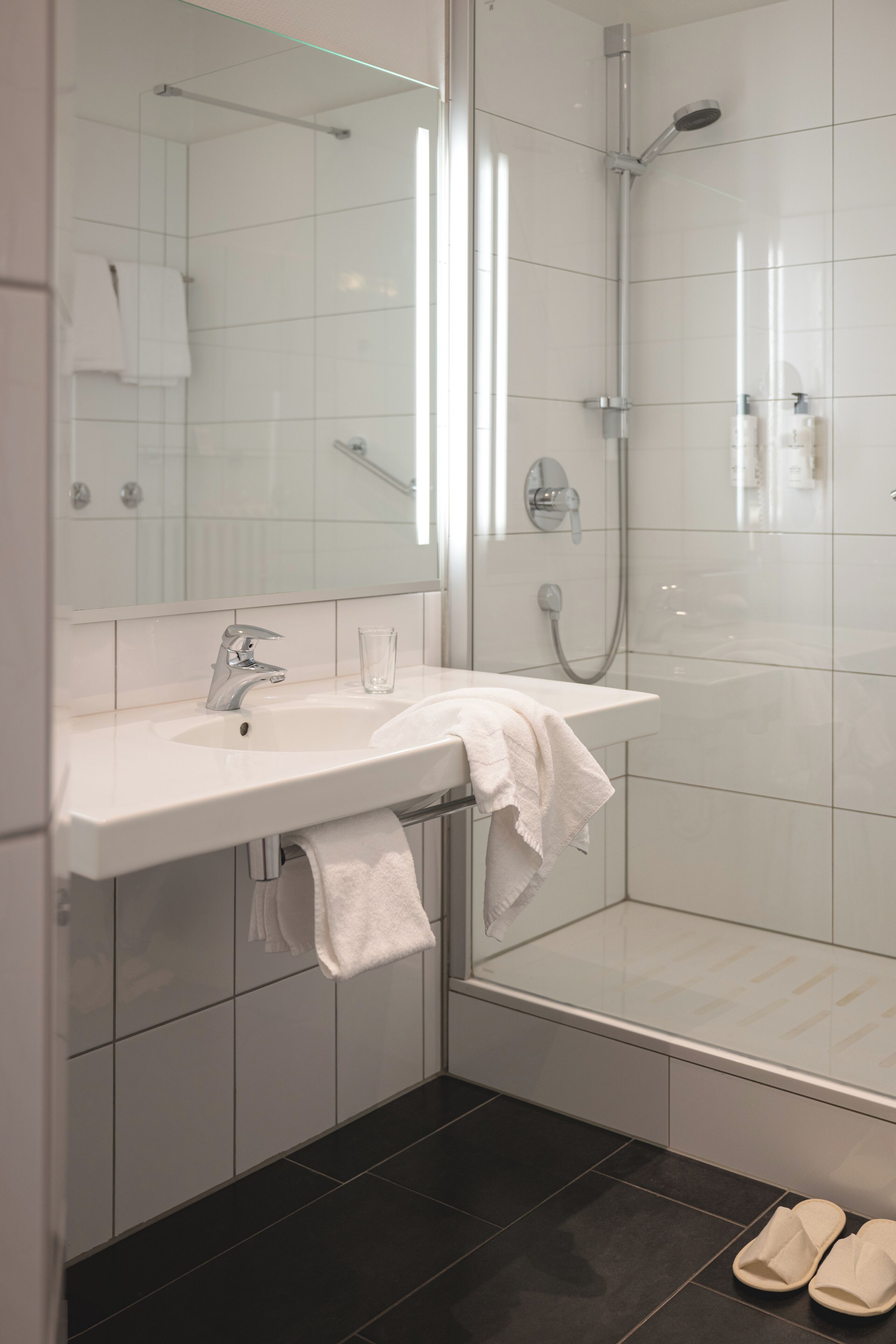 A modern bathroom with a white sink, mirror, and shower.