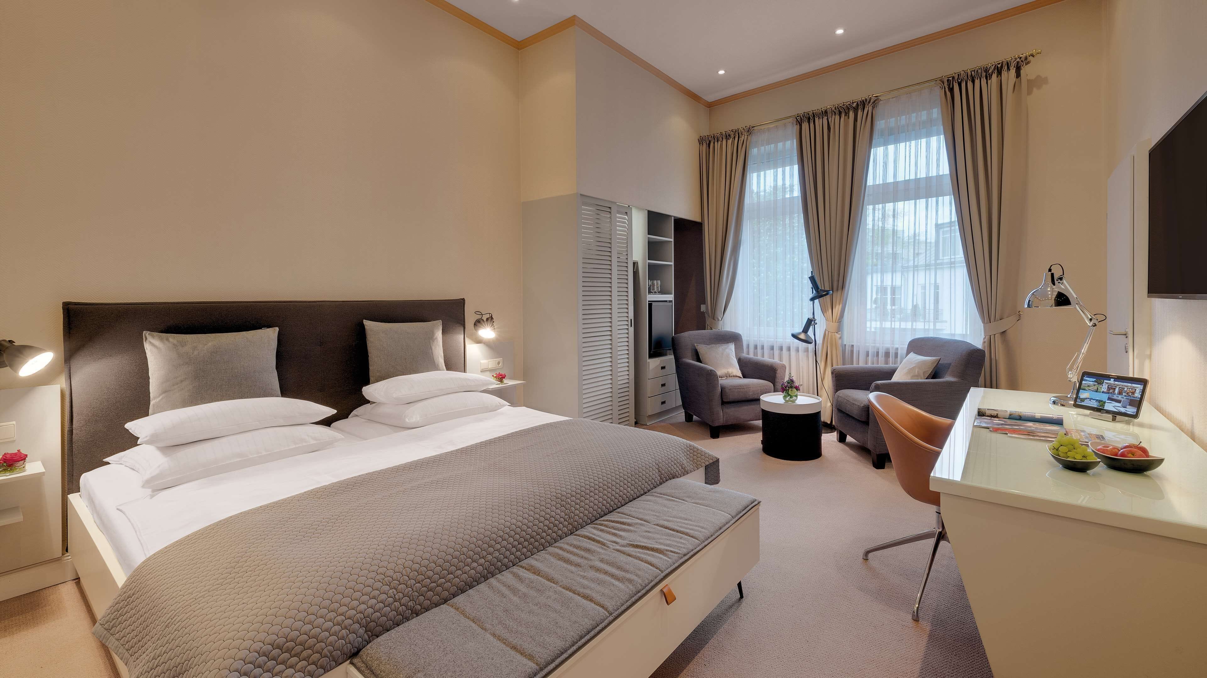 Una habitación de hotel moderna con una cama grande, dos sillones, un escritorio con una computadora portátil y un armario.