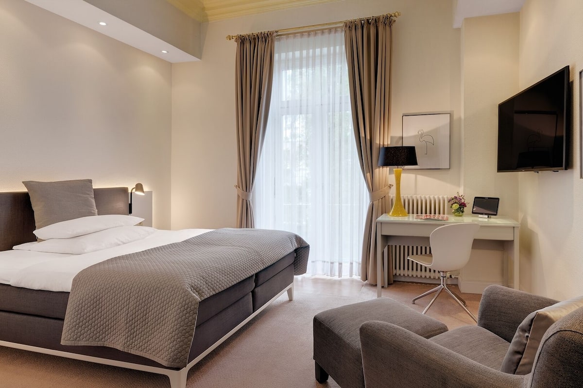 A modern hotel room with a bed, desk, chair, and artwork.