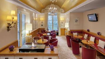 A hotel lobby with a central seating area, a fireplace, and a large window with curtains.