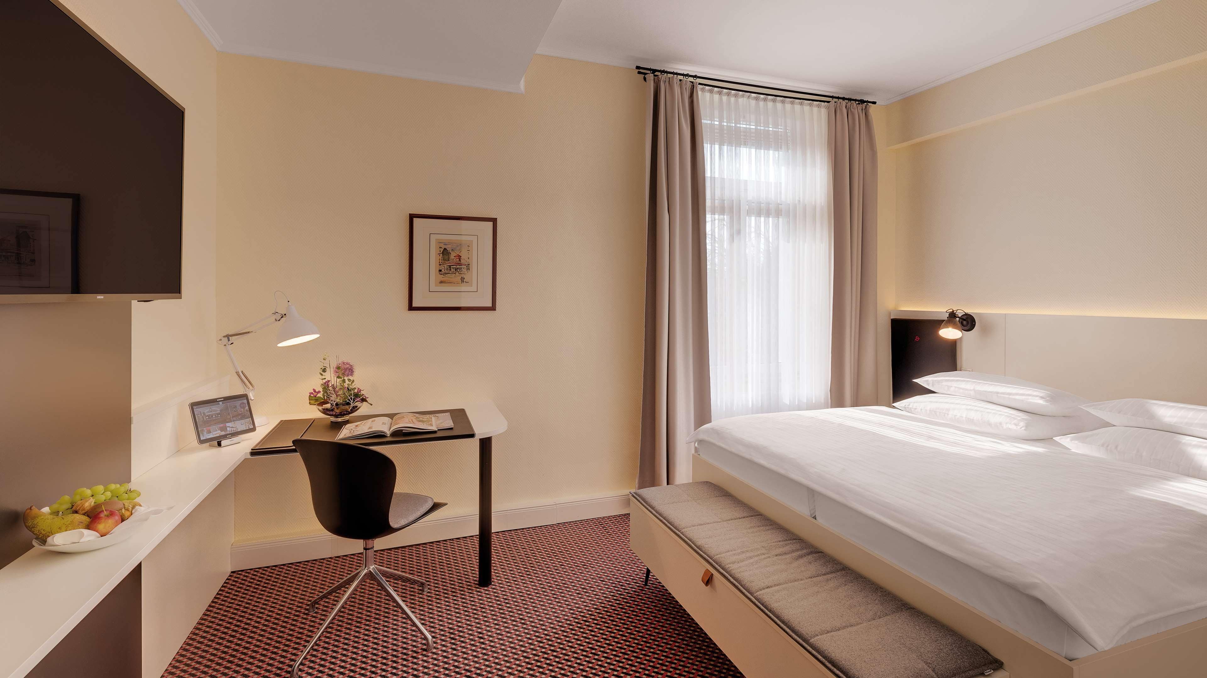 Habitación de hotel con cama, escritorio, silla y una mesita con frutas.