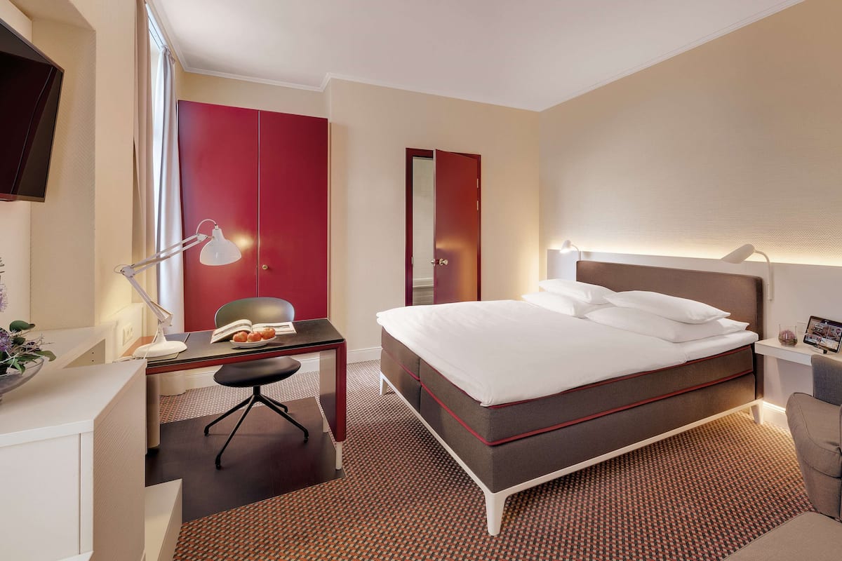 A hotel room with a bed, desk, chair, and a TV.