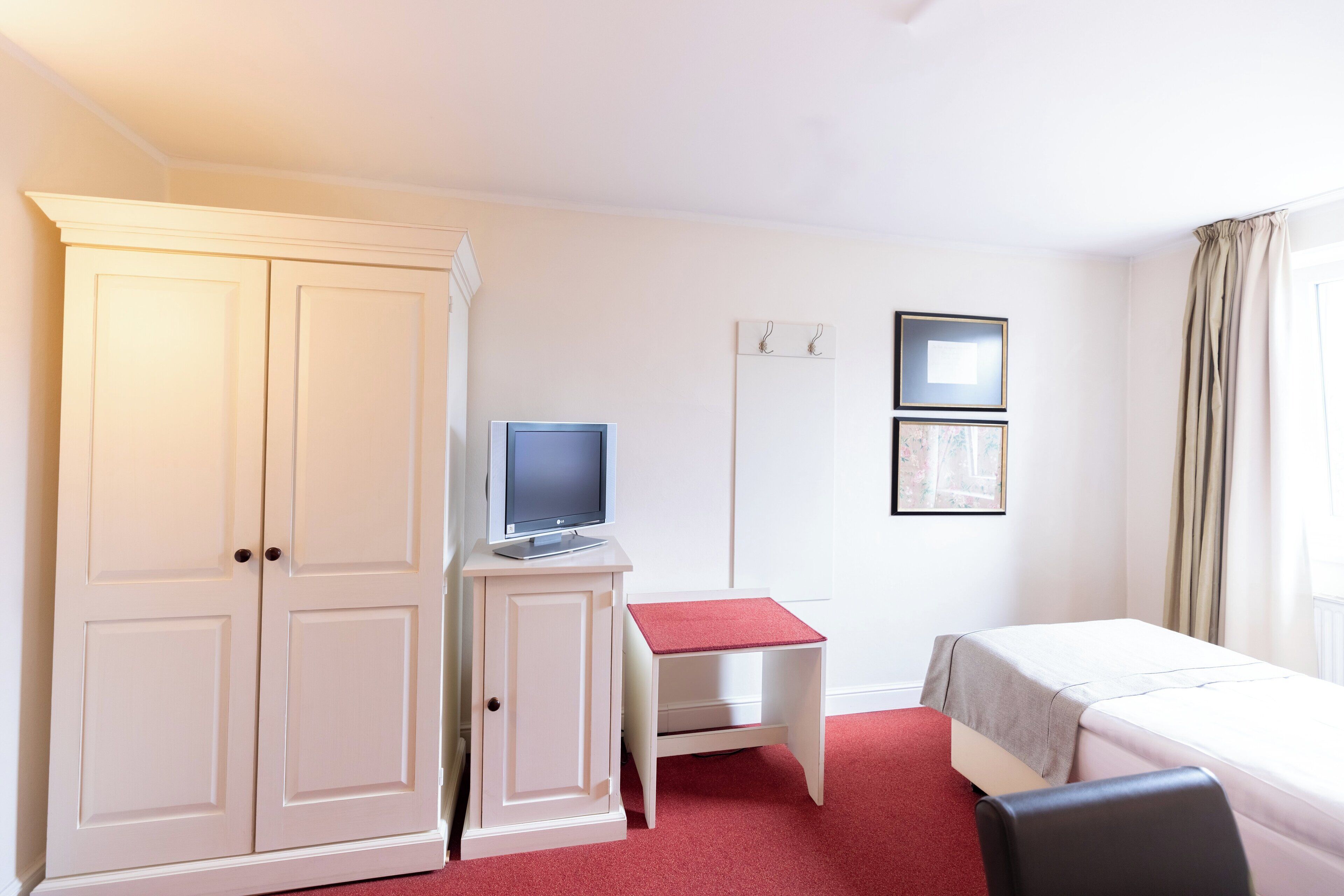 Una habitación de hotel con armario, escritorio, cama y una mesita.