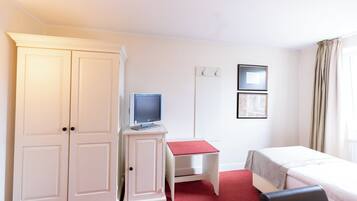 Una habitación de hotel con armario, escritorio, cama y una mesita.