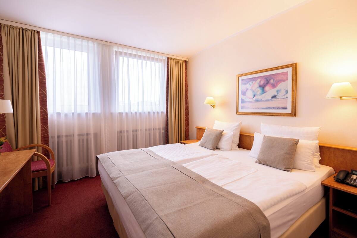 A hotel room with a large bed, a desk, and a chair. There are two bedside tables with lamps and a painting on the wall.