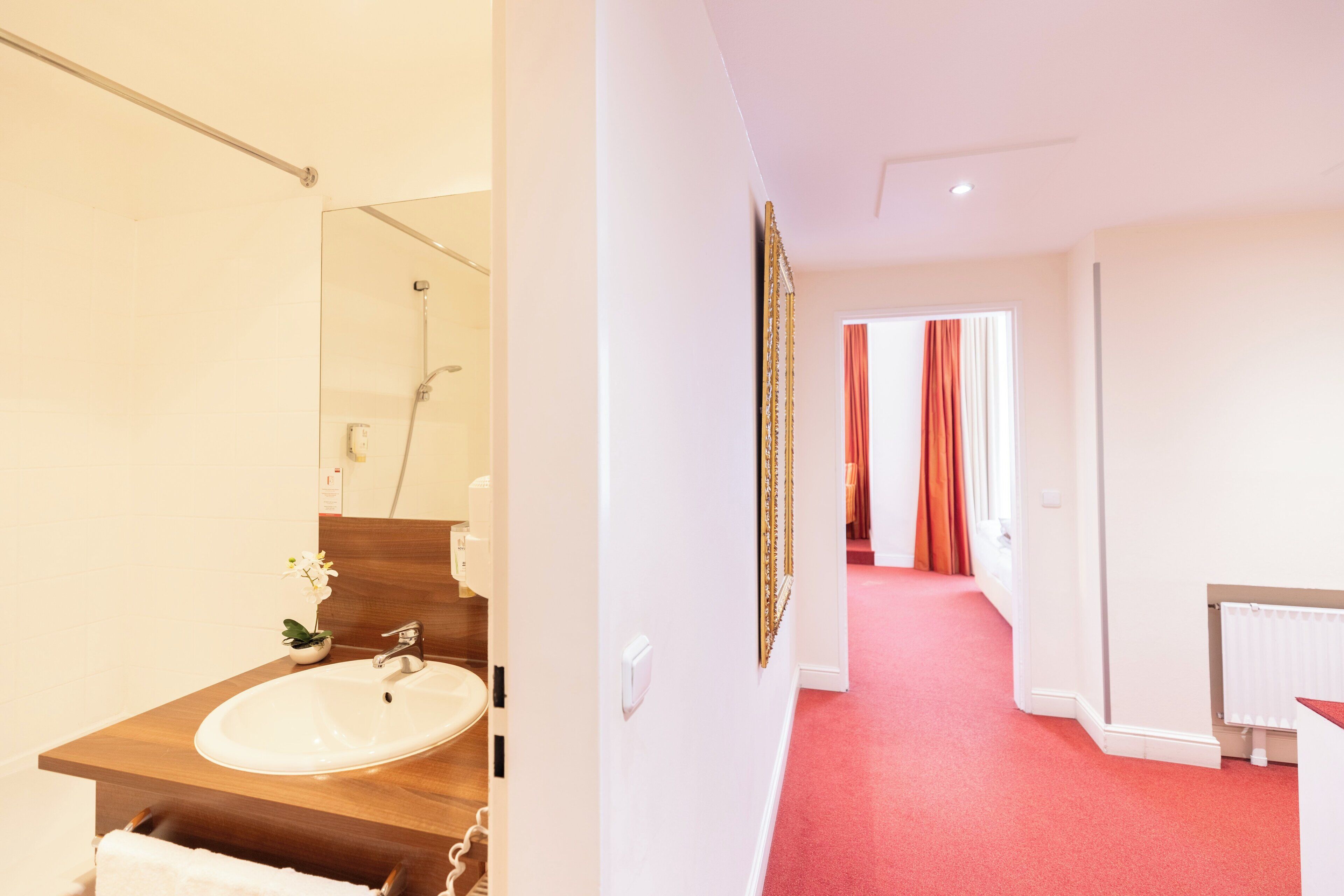 Een moderne badkamer met een witte wasbak, een houten aanrechtblad en een grote spiegel. In de achtergrond is een douche zichtbaar.