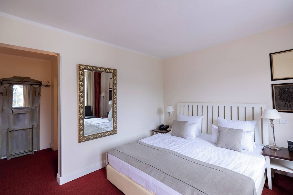 A hotel room with a large bed, a nightstand, a mirror, and a wardrobe.