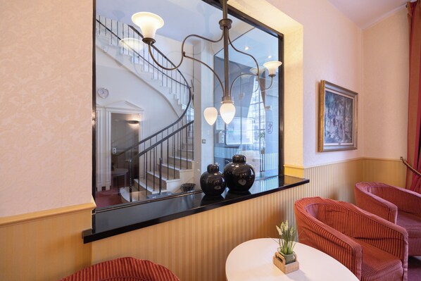 A hotel lobby with a curved black reception desk, a spiral staircase, and red upholstered chairs. - Hotel Bremer Haus (Bremen)