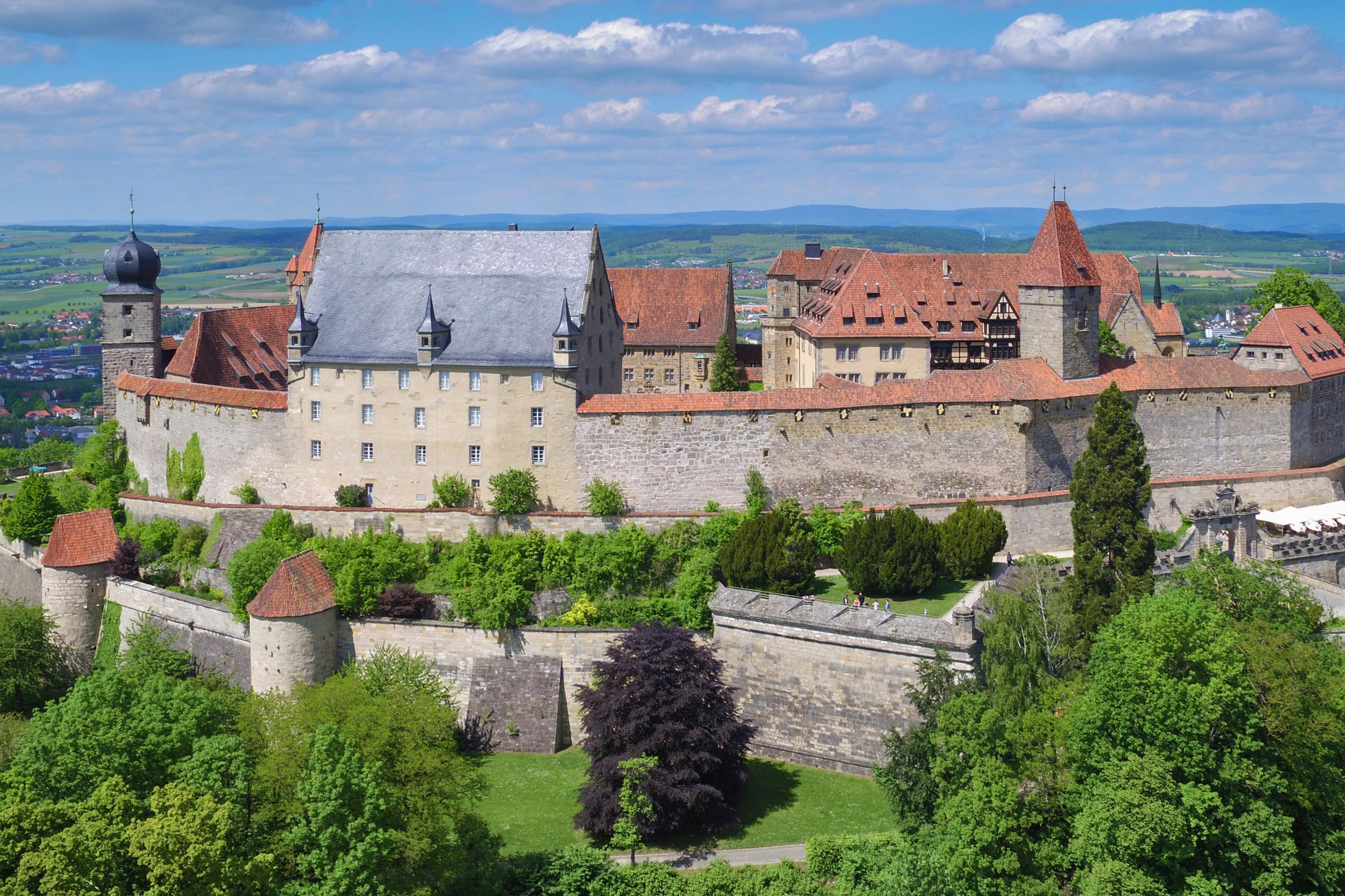 Eine historische Burg mit mehreren Türmen, einer befestigten Mauer und üppigem Grün.