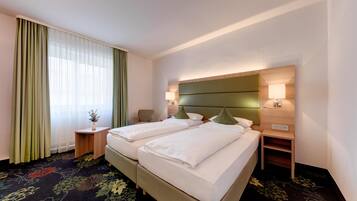 A hotel room with two beds, a nightstand, a lamp, and a window with curtains.