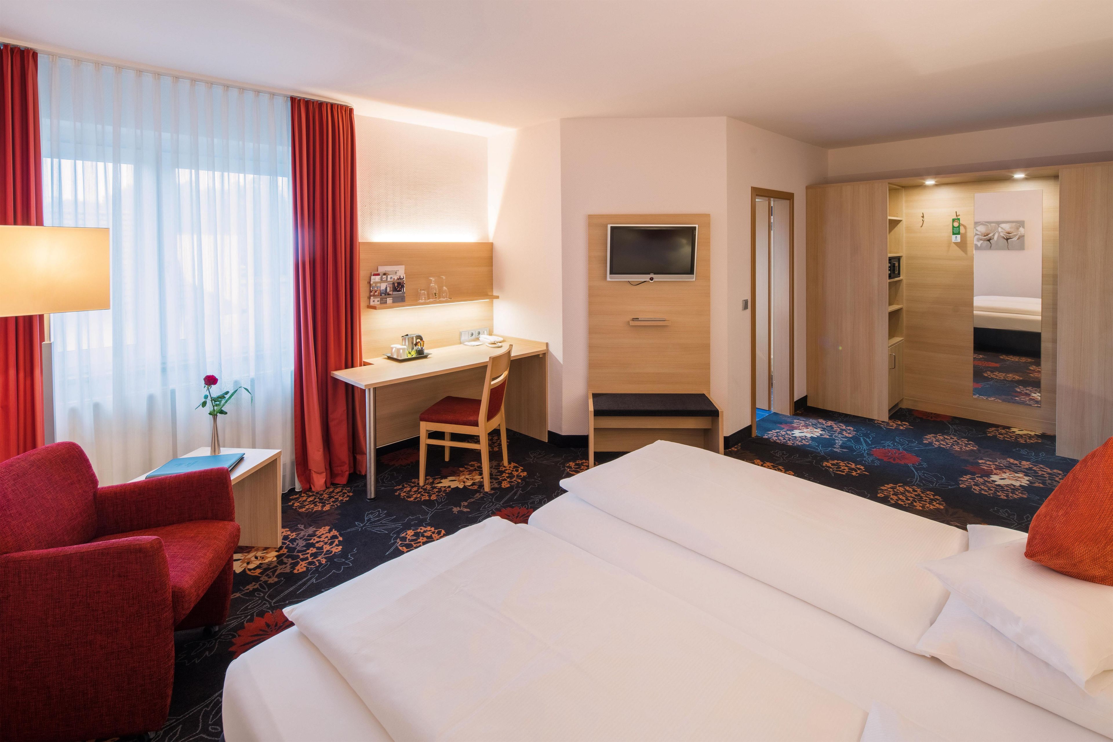 A hotel room with a bed, desk, chair, and a television.