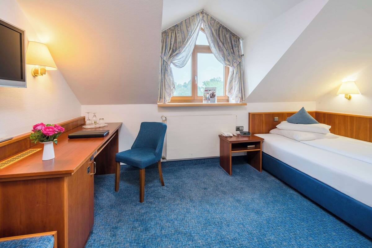Une chambre d’hôtel équipée d’un bureau, d’une chaise, d’un lit et d’une fenêtre avec des rideaux.