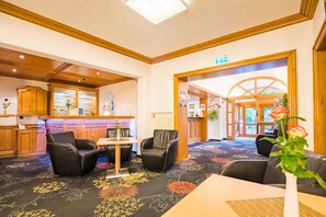 A hotel lobby with a reception desk, seating area, and a view of the outdoor area through a glass door. - Best Western Blankenburg Hotel (Coburg)