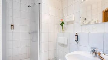 Ein modernes Badezimmer mit Duschkabine aus Glas, einem weißen Waschbecken und einem Spiegel darüber.