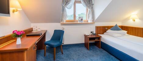 Una habitación de hotel con escritorio, silla, cama y ventana con cortinas.