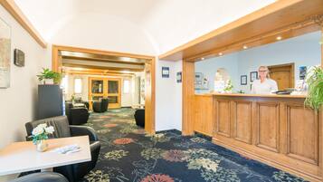 Un hall d’hôtel comprenant un comptoir d’accueil, un espace salon et un sol recouvert de moquette.