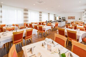 A hotel dining area with multiple tables, chairs, and a central buffet station. - Best Western Blankenburg Hotel (Coburg)