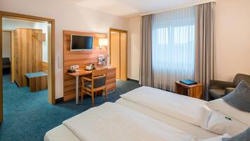 Ein Hotelzimmer mit einem Bett, einem Schreibtisch, einem Stuhl, einem Fernseher und einem fensterbepflanzten Fenster.