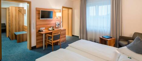 A hotel room with a bed, a desk, a chair, a television, and a window with curtains.
