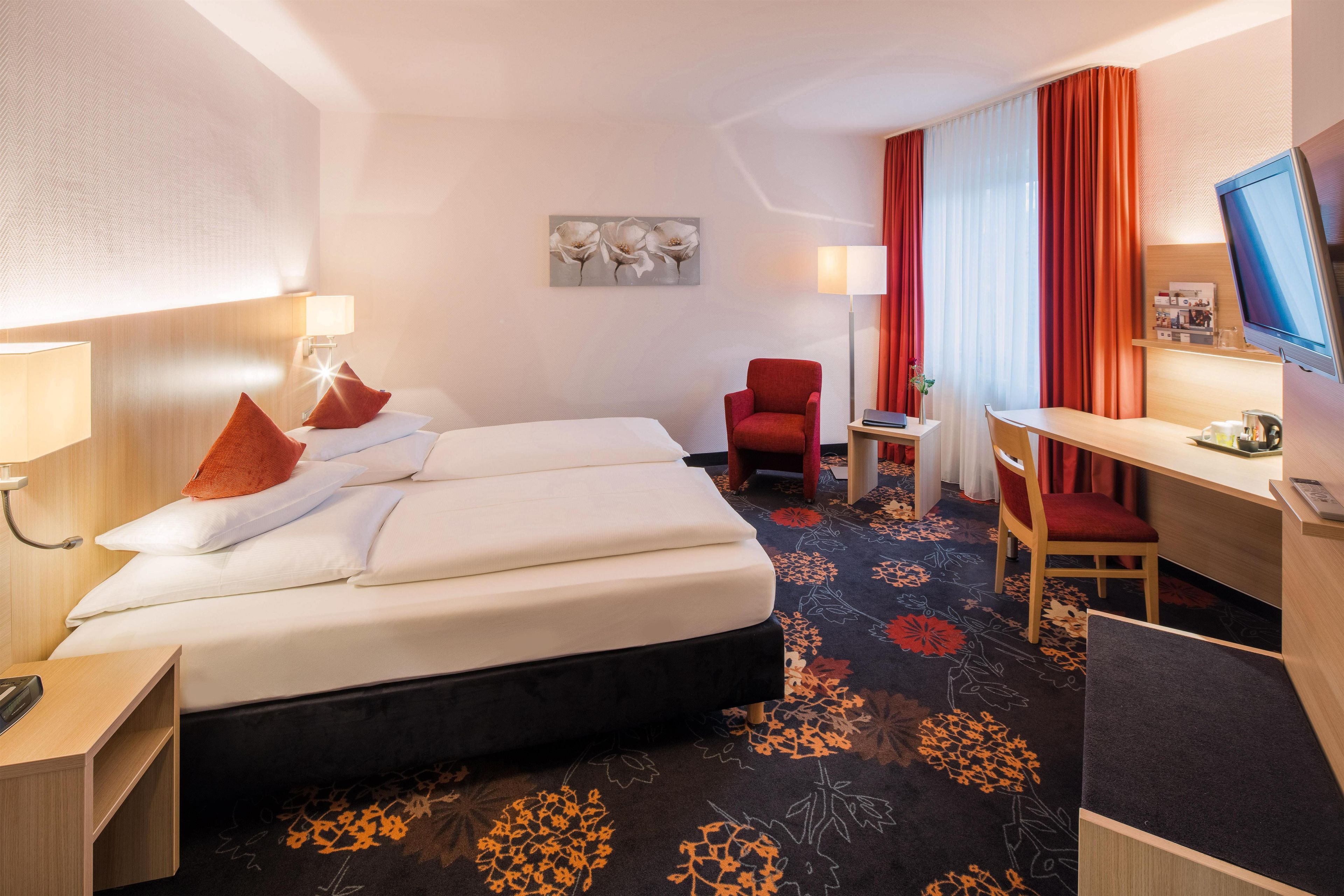 Een hotelkamer met een bed, een bureau, een stoel, een televisie en een schilderij aan de muur.