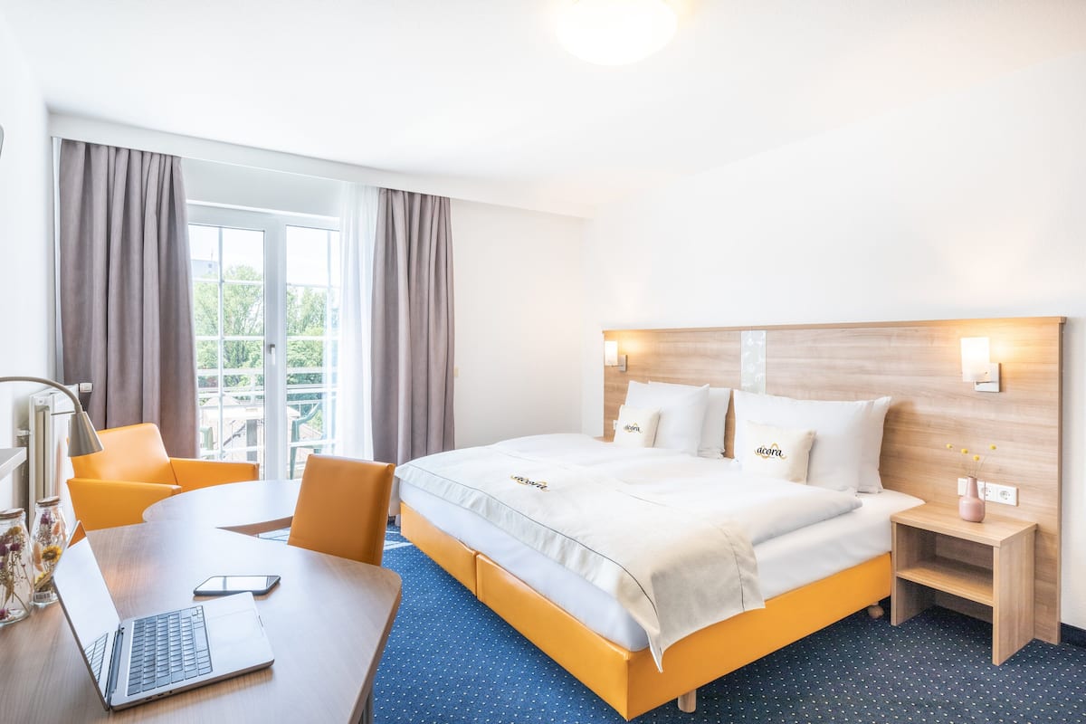 Hotellihuone, jossa on sänky, työpöytä kannettavalla tietokoneella, tuoli, yöpöytä ja lamppu.