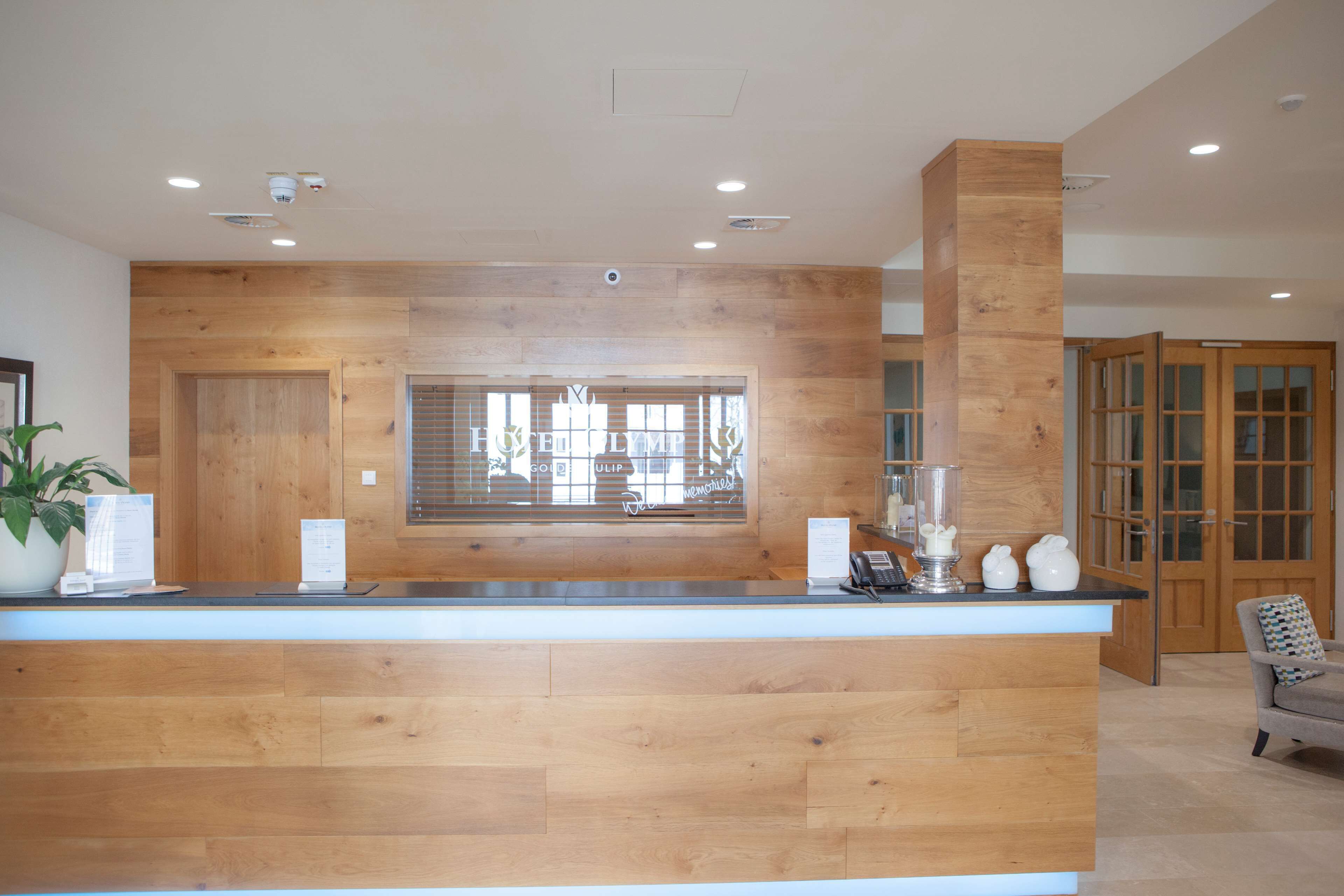 Un mostrador de recepción con detalles de madera, una planta en maceta y una ventana con persianas.