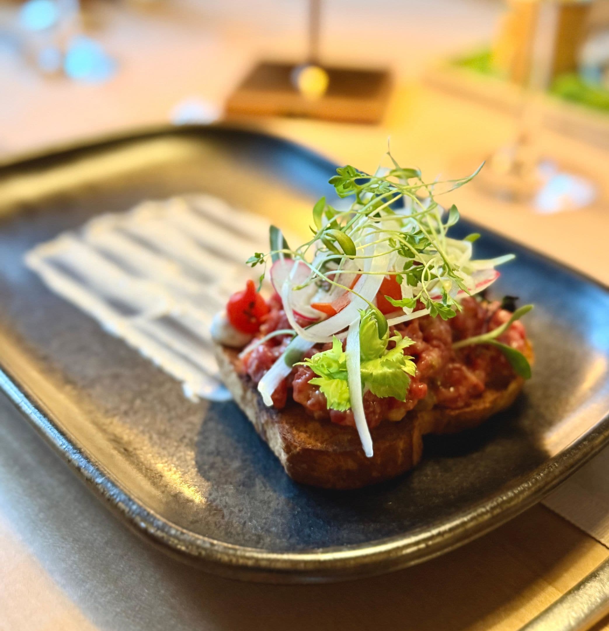 Ein Teller mit dunklem Hintergrund, belegt mit Brot, roter Soße, Grünzeug und einer weißen Soße.