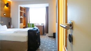 A hotel room with a bed, a desk, a wardrobe, and a suitcase.