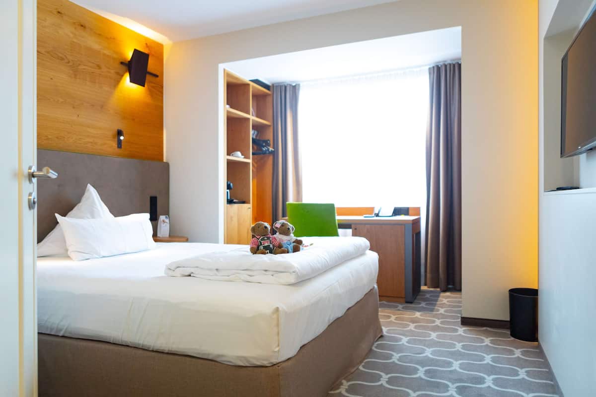 Habitación de hotel con una cama grande, un escritorio y un televisor.