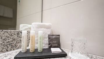 A bathroom counter with toiletries including body lotion, shampoo, and shower gel, a soap bar, and a glass.