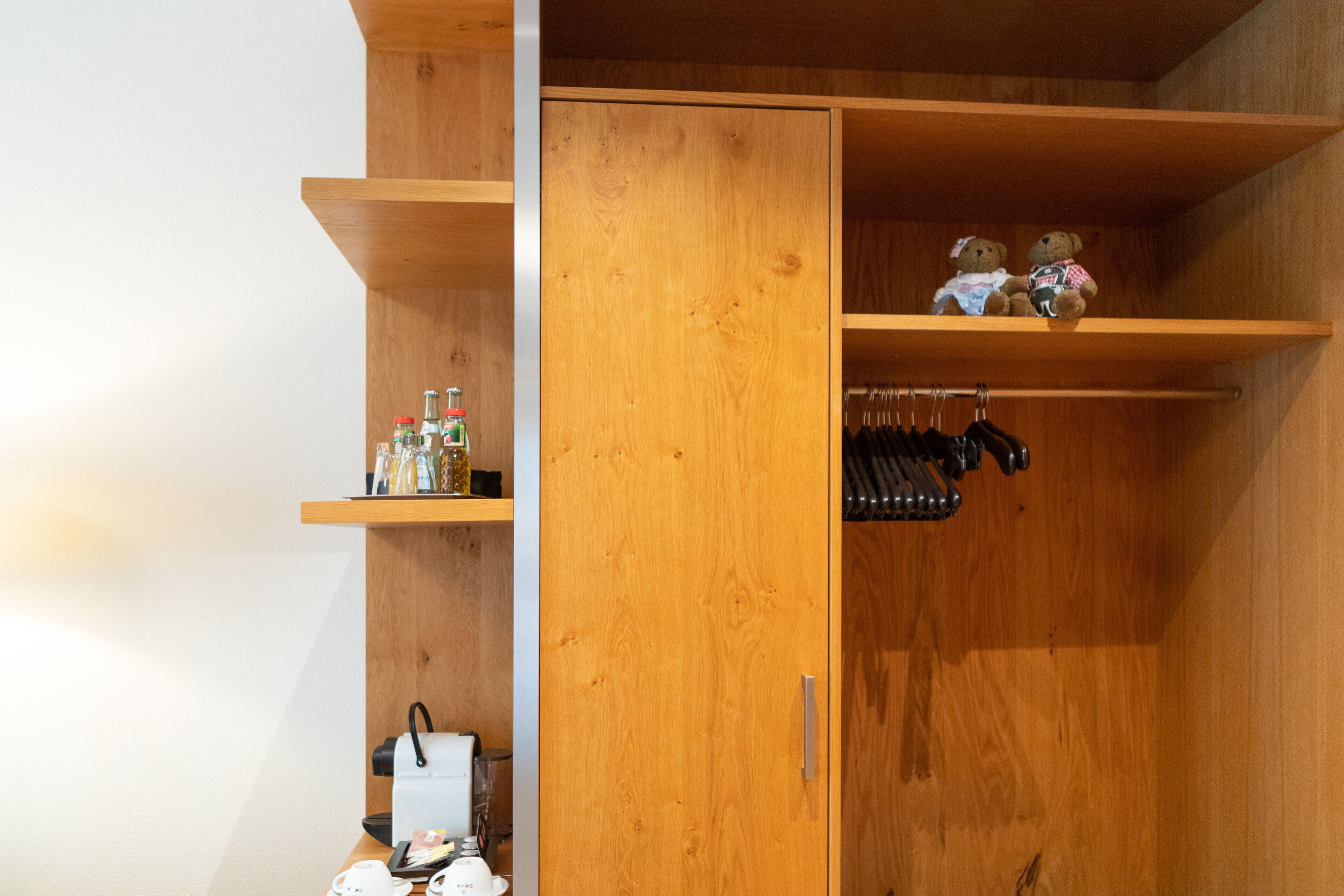 A wooden wardrobe with two shelves, one holding bottles and the other with hanging items.