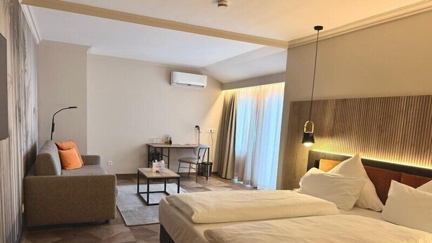 Een hotelkamer met twee bedden, een bank, een eettafeltje en een bureau met stoel.