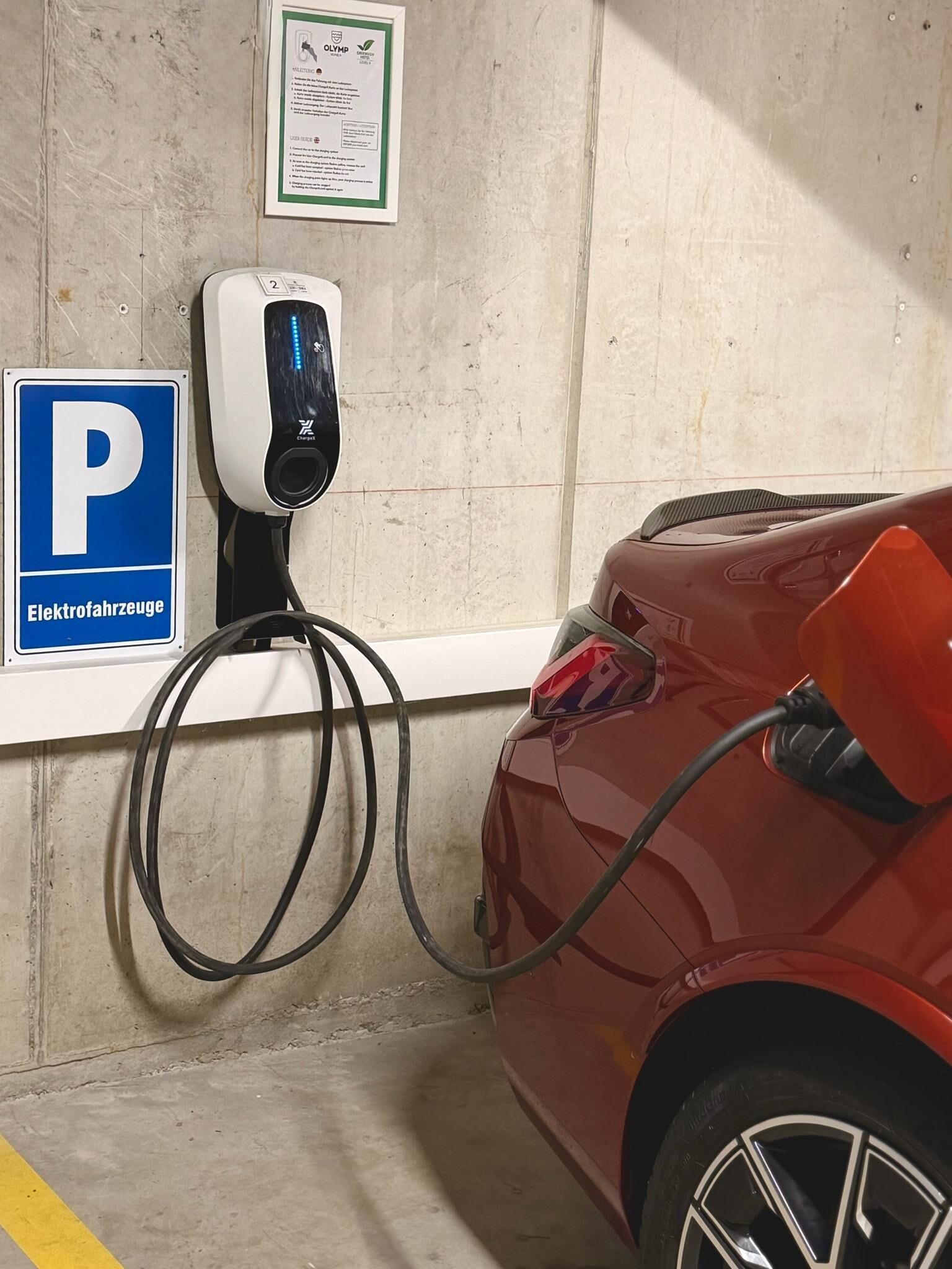 Une place de stationnement équipée d’une borne de recharge pour véhicules électriques, un panneau de signalisation de stationnement bleu et un avis affiché sur le mur.