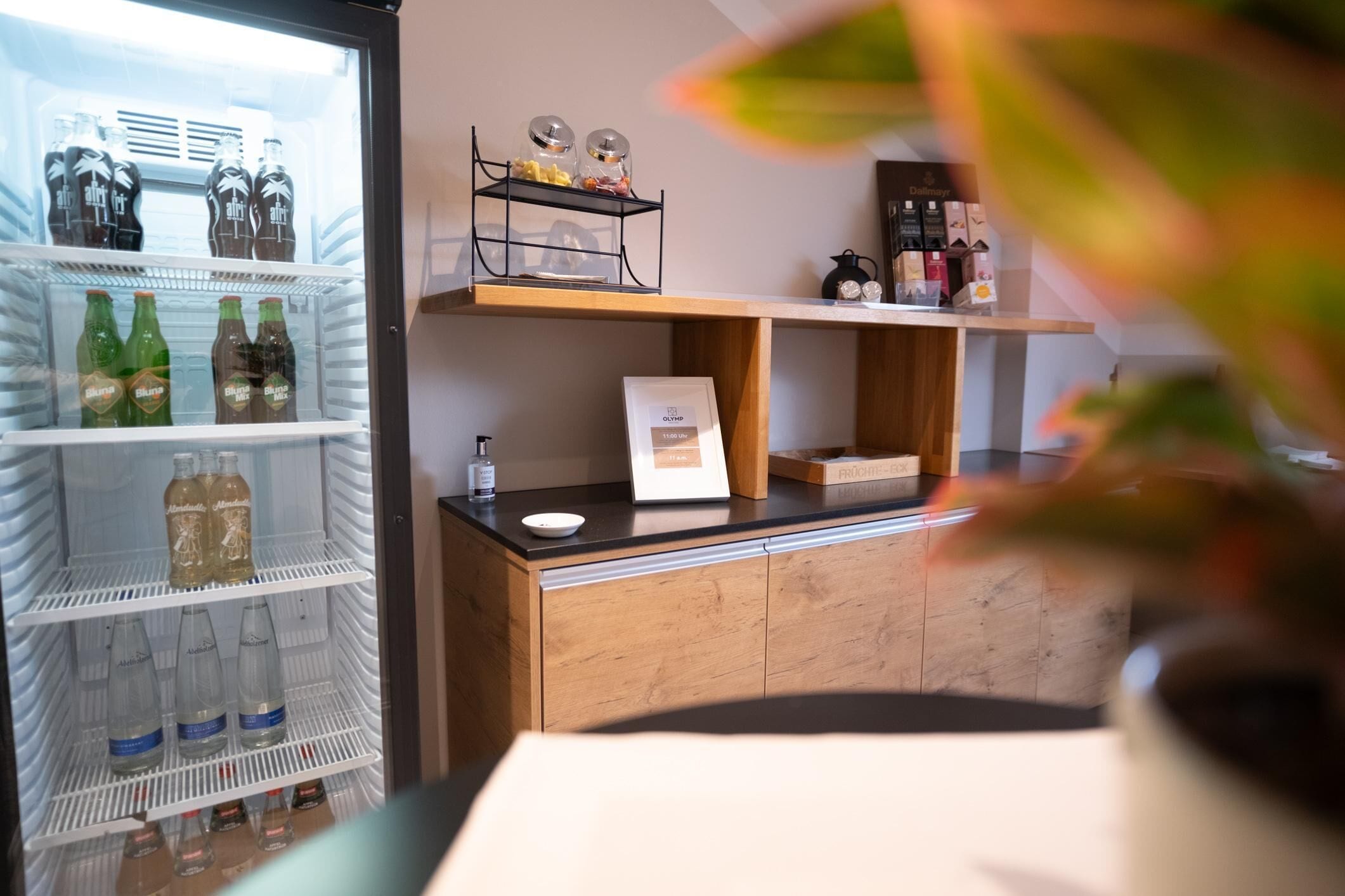 Un réfrigérateur rempli de boissons, une machine à café et une étagère avec des bocaux et un tableau encadré.