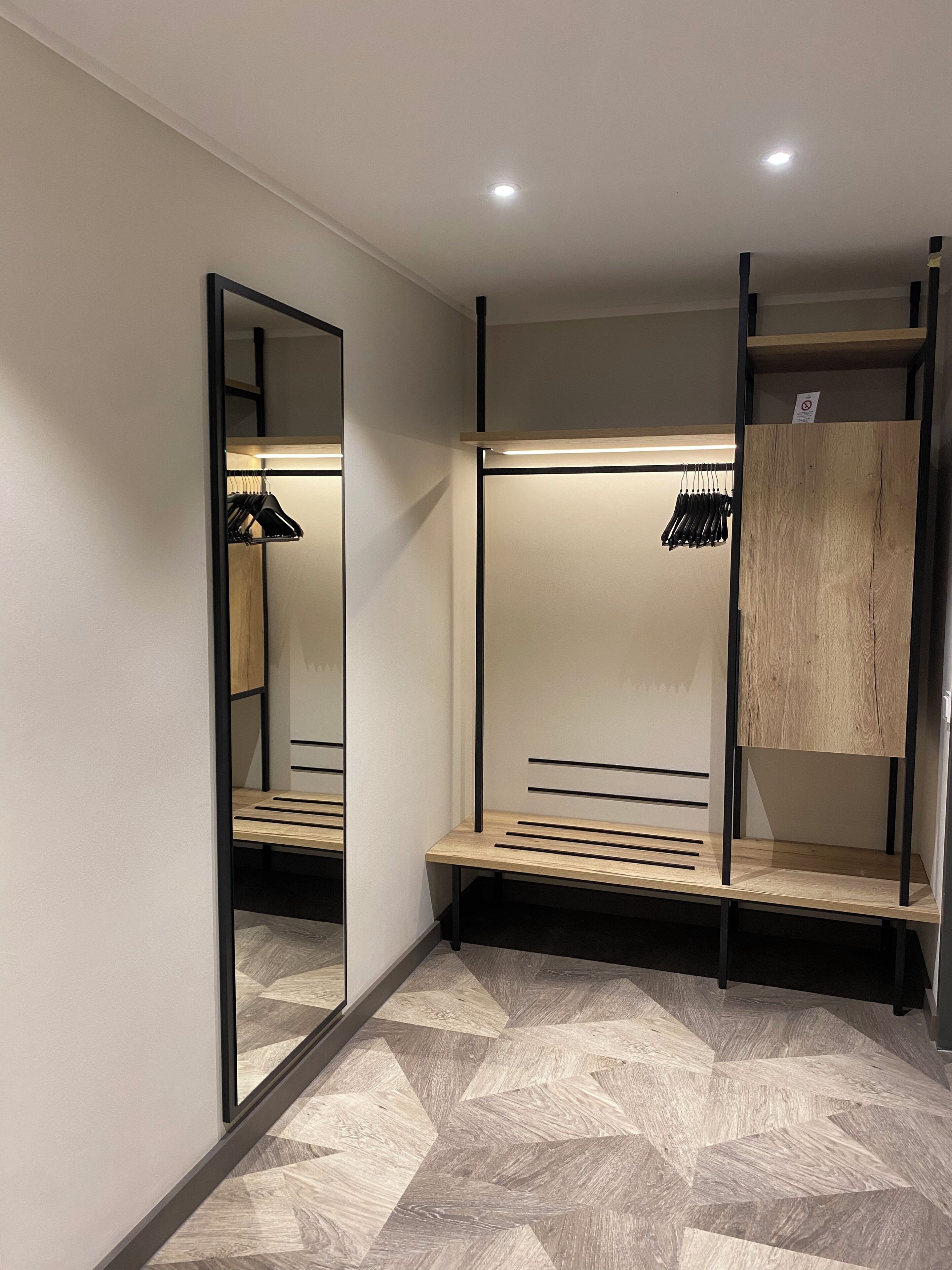 Una cabina armadio moderna e luminosa, con pareti a specchio, panche in legno e spazio per appendere i vestiti.