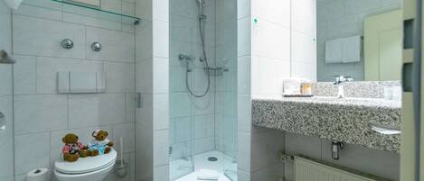 A modern bathroom with a glass-enclosed shower, a toilet with teddy bears, and a granite countertop.