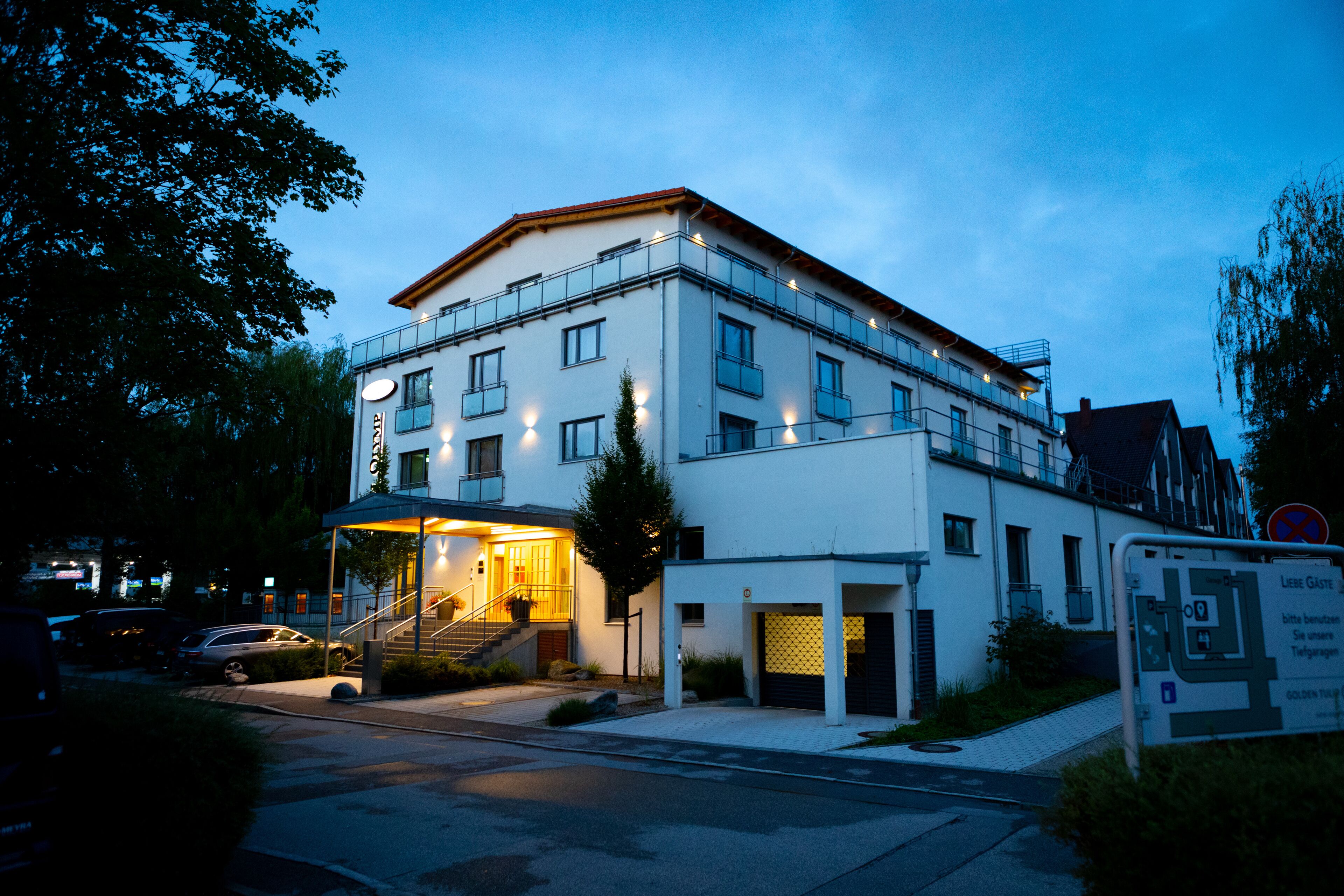 A modern hotel with a glass facade, a covered entrance, and a sign indicating amenities.