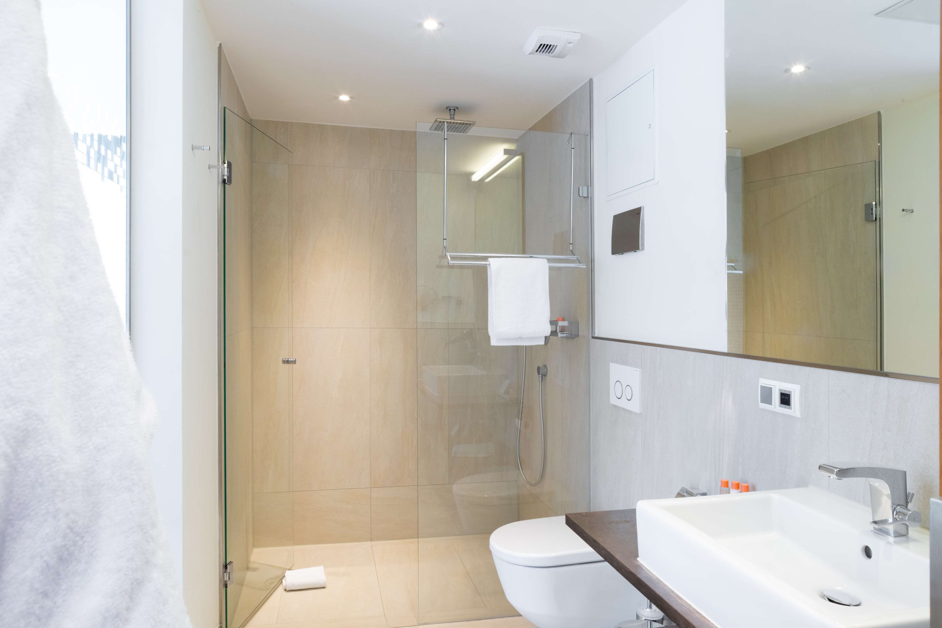 Un bagno moderno con doccia vetrata, un water bianco e un lavabo spazioso con uno specchio sopra.