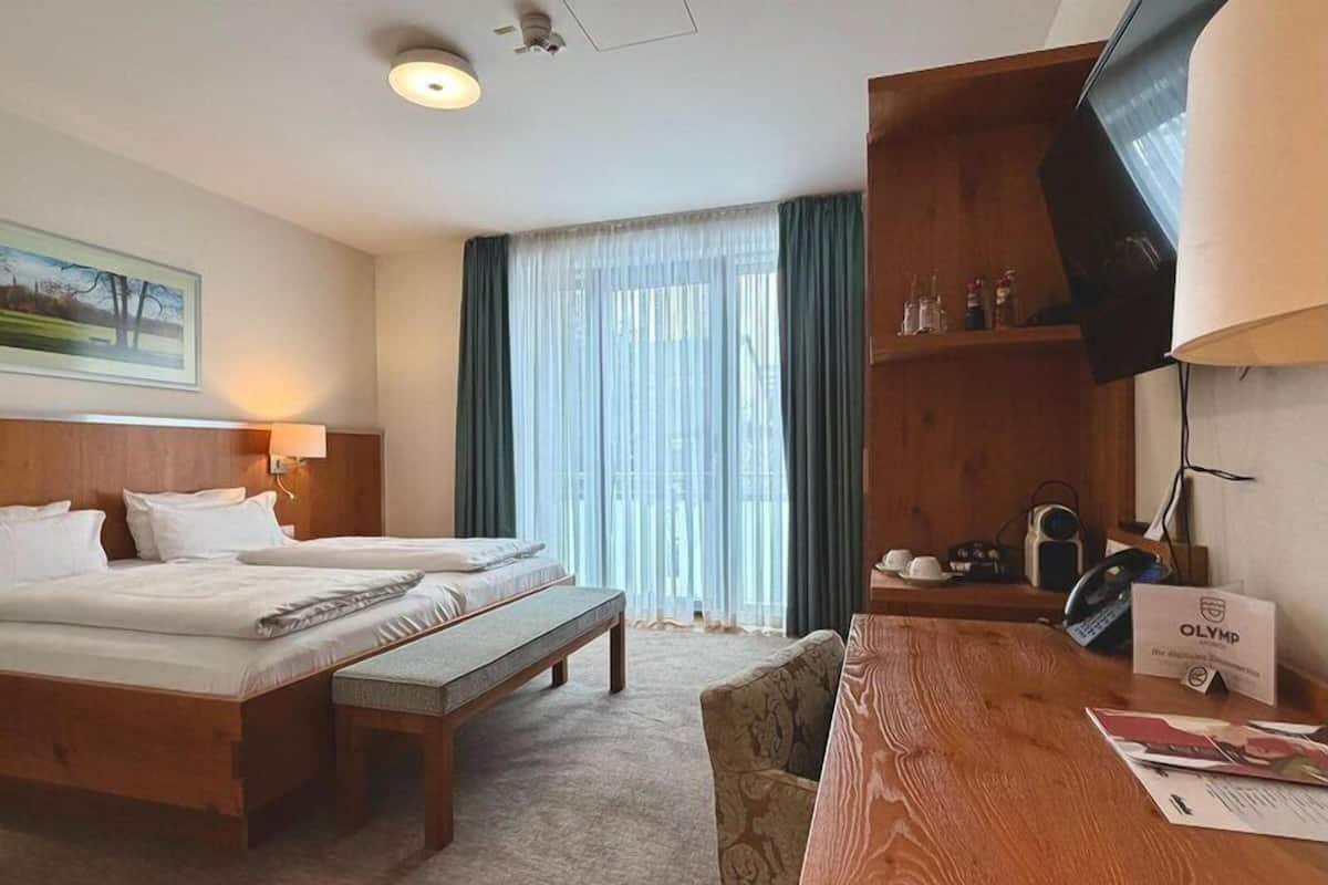 Habitación de hotel con cama, escritorio, silla, televisión y ventana con cortinas.