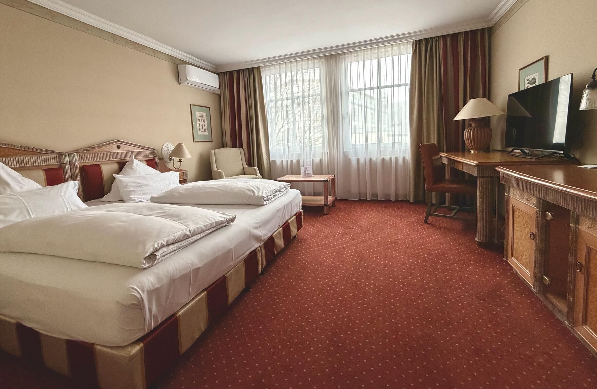 Une chambre d’hôtel avec deux lits, un bureau avec une télévision, une chaise et une fenêtre avec des rideaux.