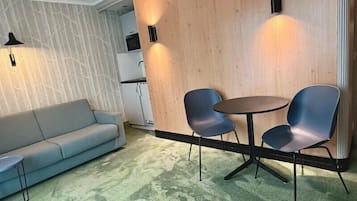 A room with a sofa, two chairs, a small table, a wooden partition, and a kitchen area.